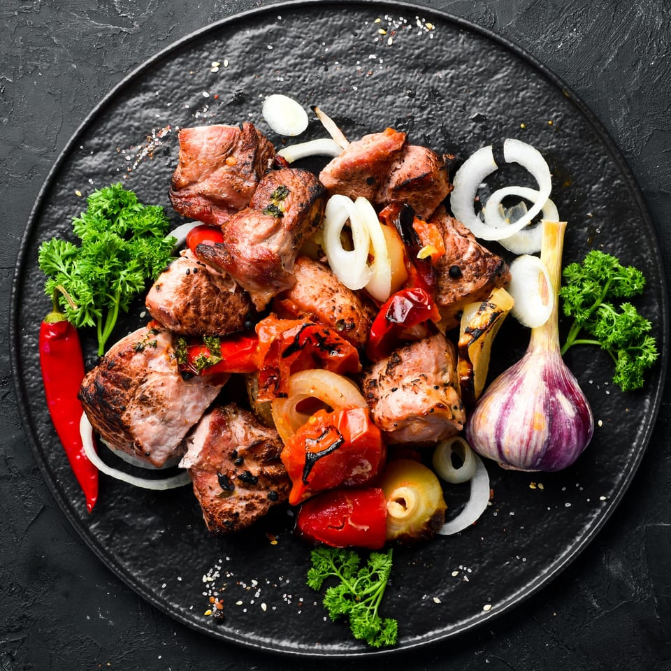 Grilled Aziz Hot Chicken & Kebab with peppers, onions, parsley, and garlic on a black plate.