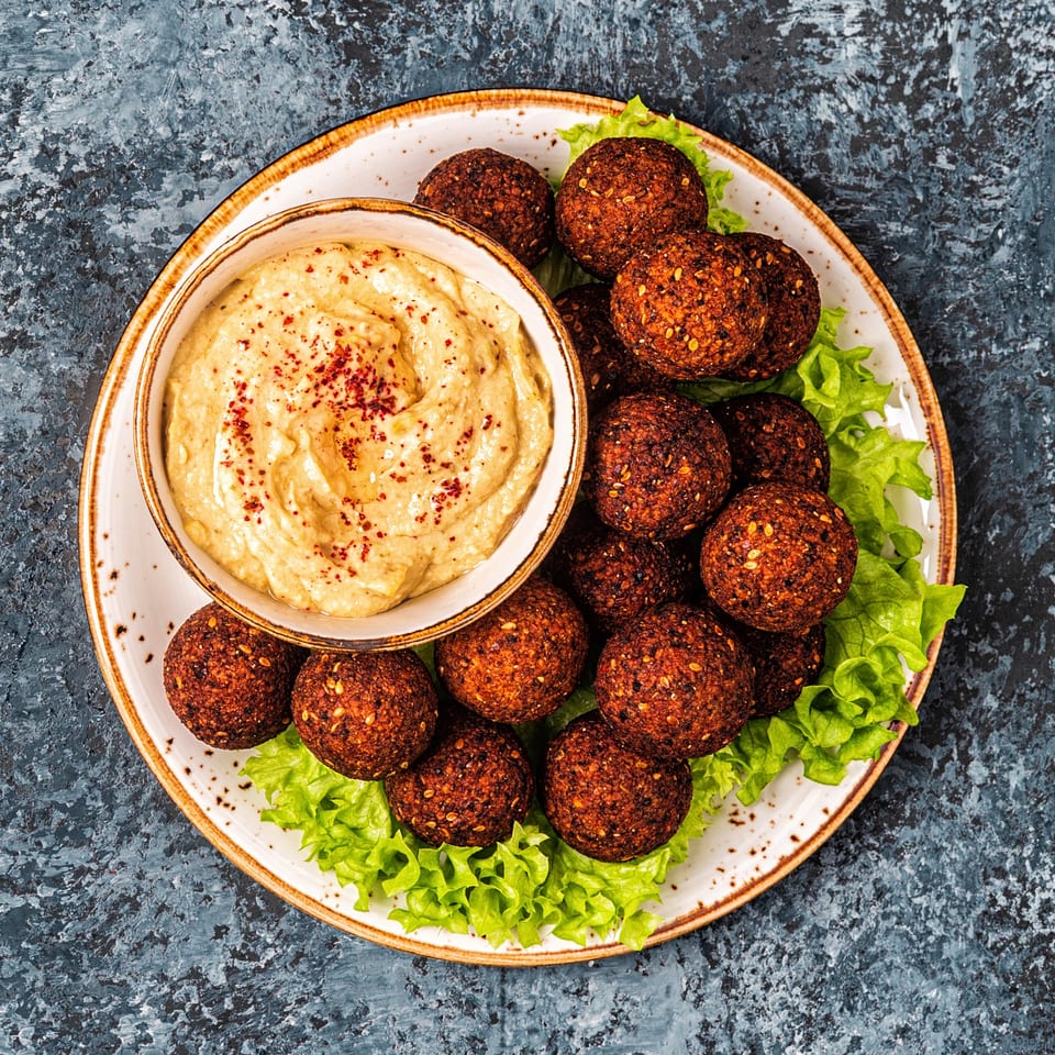 A plate of Aziz Hot Chicken & Kebab falafel with hummus and lettuce on a dark background.